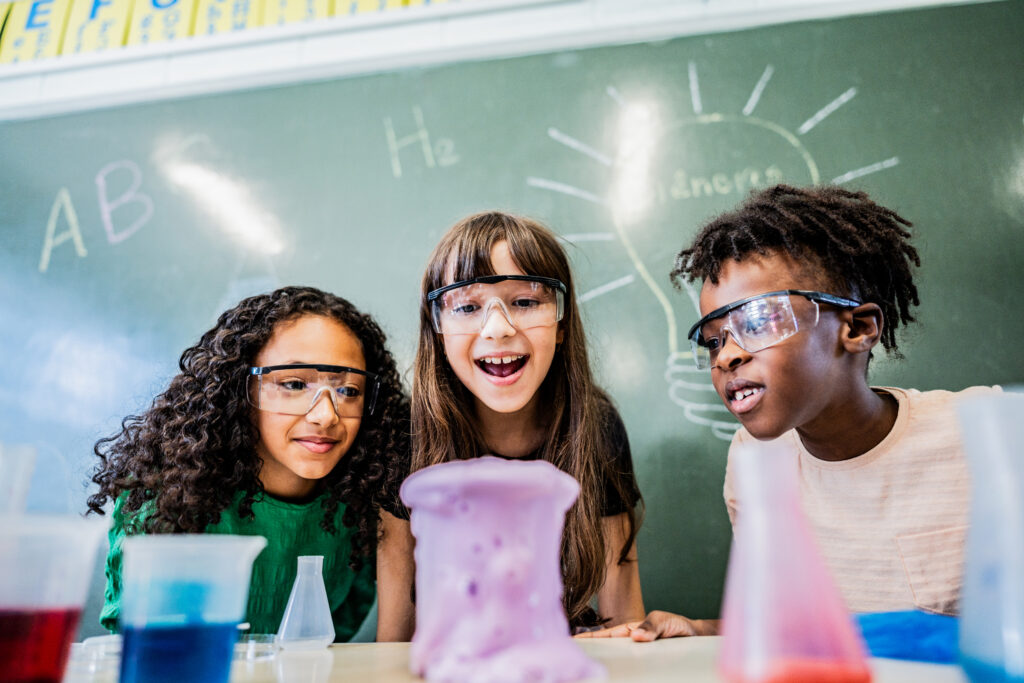 Three elementary school students look at a bubbling beaker.